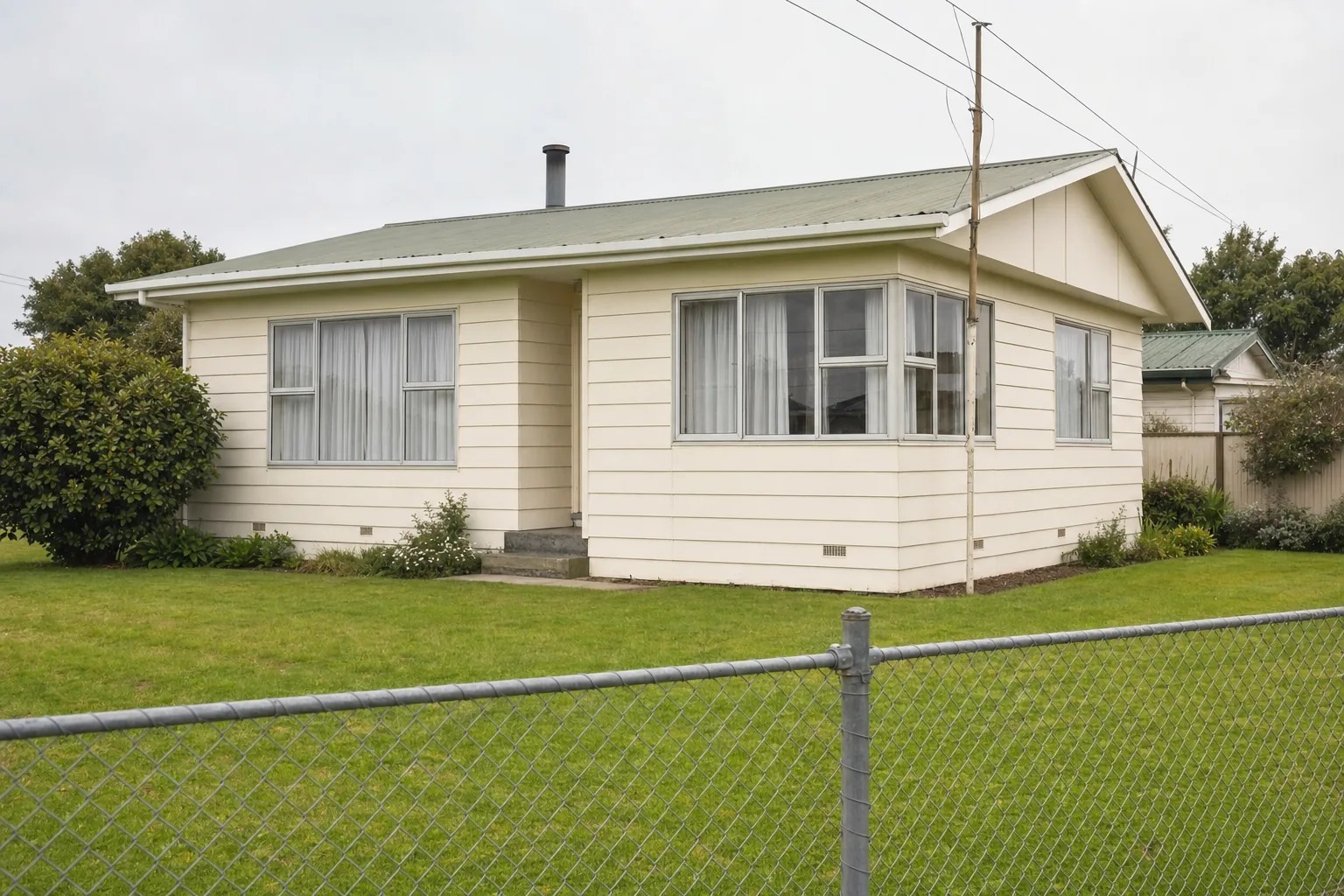 A modest post-war single-storey house with aluminium windows and a chain-link fence